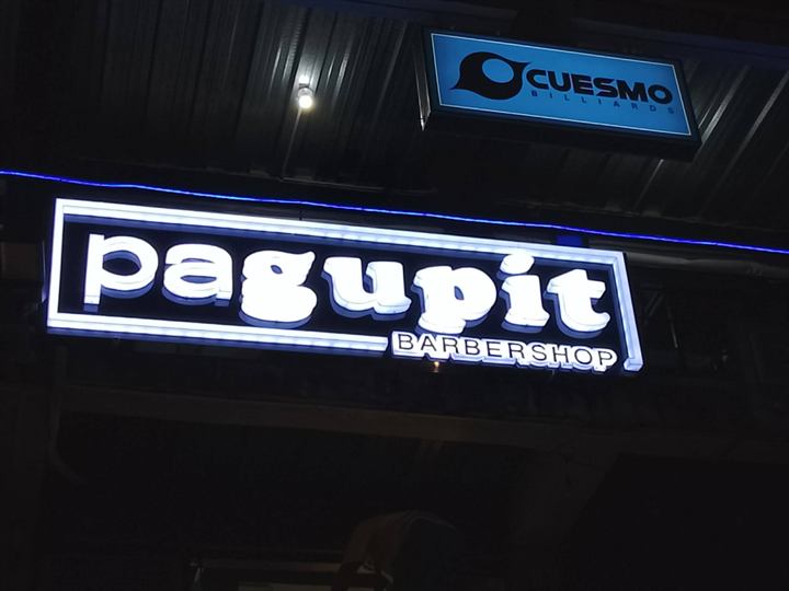Pagupit Barbershop white lit acrylic sign glowing at night